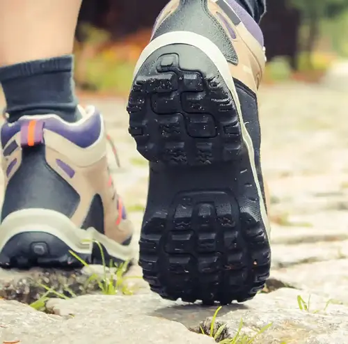 Wanderschuhe auf Kopfsteinpflaster. Die Person auf dem Bild läuft durch ein Waldstück.