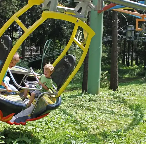 Zwei Kinder fahren mit dem Wie-Flyer, einer Attraktion der Wiegand Erlebnisberge, durch die Baumlandschaft. Der Betreiber von Sommerrodelbahnen bietet dieses schwebende Fahrgeschäft für ein besonderes Freizeiterlebnis