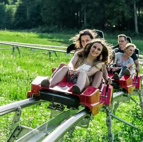 Mehrere Personen fahren mit hoher Geschwindigkeit die Sommerrodelbahn der Wiegand Erlebnisberge hinunter. Der Betreiber von Sommerrodelbahnen bietet actionreiche Fahrten durch grüne Landschaften