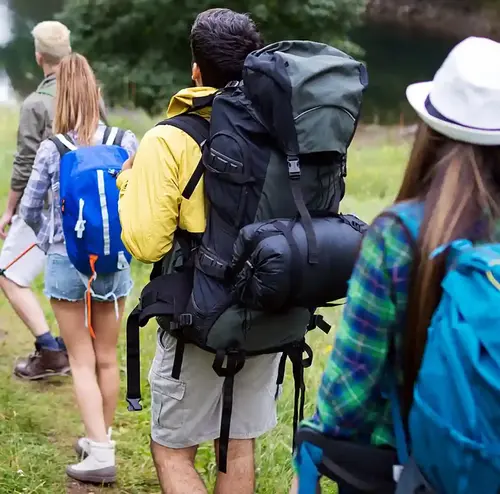 Eine Gruppe junger Erwachsener läuft über einen kleinen Pfad in Richtung eines Sees. Sie haben Rucksäcke und Wanderklamotten an.