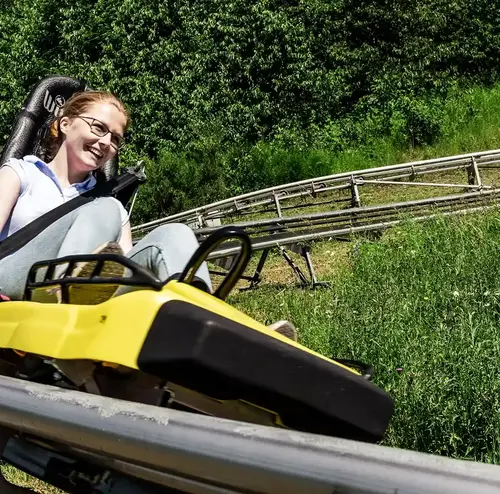 Eine Frau fährt lachend die Sommerrodelbahn der Wiegand Erlebnisberge hinunter. Der Betreiber von Sommerrodelbahnen bietet rasantes Vergnügen auf einer modernen Schienenstrecke durch die Natur