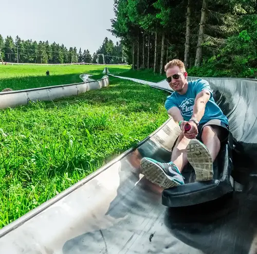 Ein Mann fährt mit hoher Geschwindigkeit die Sommerrodelbahn der Wiegand Erlebnisberge hinunter. Der Betreiber von Sommerrodelbahnen bietet rasanten Freizeitspaß inmitten der Natur
