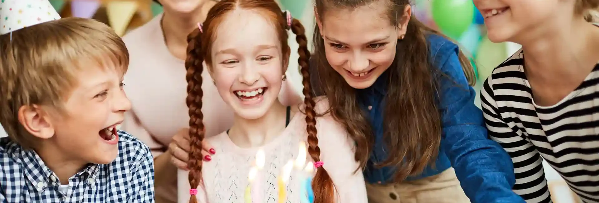 Eine Mutter feiert mit Kindern einen Kindegeburtstag. Die Kinder sind alle nah zusammen und lachen. Sie schauen alle auf den Kuchen, der vor ihnen auf dem Tisch steht.