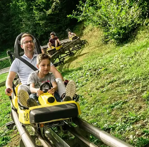 Ein Vater und sein Kind fahren auf einer Sommerrodelbahn der Wiegand Erlebnisberge durch die grüne Landschaft. Der Betreiber von Sommerrodelbahnen bietet rasantes Vergnügen für die ganze Familie