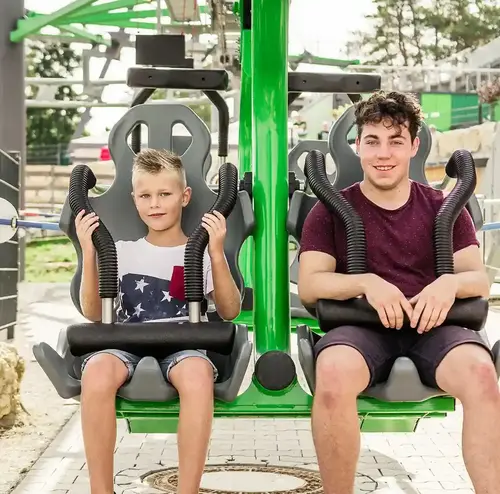Ein Junge und ein Mann sitzen in der Startposition des Wie-Flyers der Wiegand Erlebnisberge. Der Betreiber von Sommerrodelbahnen bietet mit dieser Attraktion ein schwebendes Fahrerlebnis in luftiger Höhe