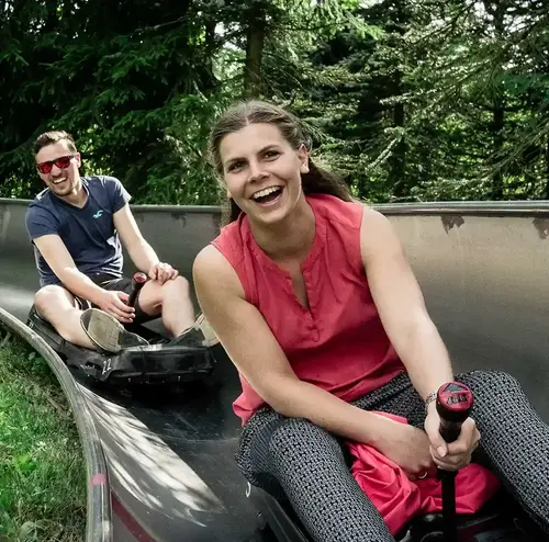 Zwei Personen fahren lachend die Sommerrodelbahn der Wiegand Erlebnisberge hinunter. Der Betreiber von Sommerrodelbahnen sorgt für rasanten Freizeitspaß in der Natur.