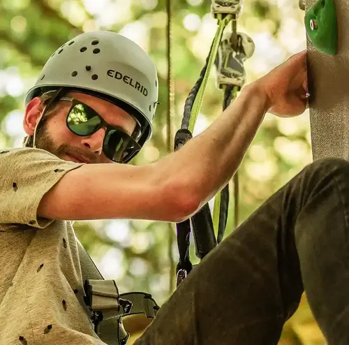 Ein Mann mit Helm und Kletterausrüstung erklimmt eine Wand im Kletterwald der Wiegand Erlebnisberge. Der Betreiber von Sommerrodelbahnen setzt auf höchste Sicherheit für Abenteuer in luftiger Höhe