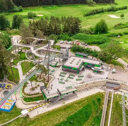 Luftaufnahme eines Freizeitparks der Wiegand Erlebnisberge, Betreiber von Sommerrodelbahnen, mit Skywalk, Kinderspielplatz und moderner Rodelbahn inmitten grüner Landschaft
