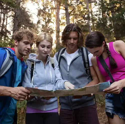eine Gruppe junger Erwachsener studiert inmitten eines Waldes eine Karte.