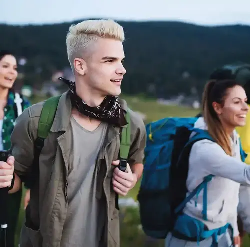 Eine Gruppe junger Erwachsener läuft durch die Natur. Sie haben Trekkingstöcke dabei uns amüsieren sich.